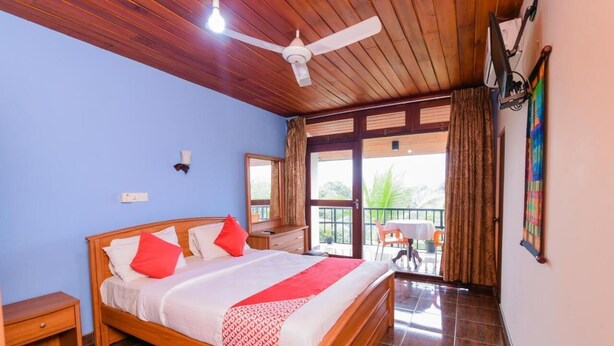 Un dormitorio con cama de madera, ventilador de techo, ventana con cortinas y vistas al exterior.