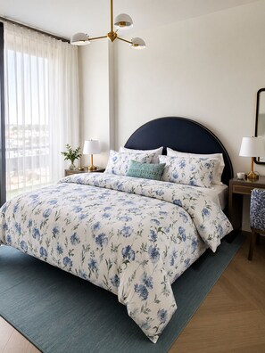 Een hotelkamer met een bed, nachtkastje, lamp, spiegel en uitzicht op de stad.