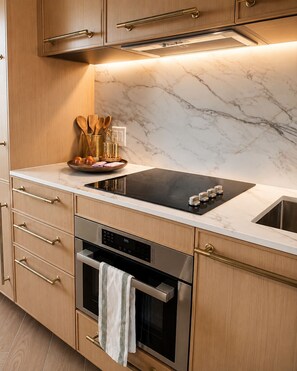 Een moderne keuken met een zwart fornuis, een roestvrijstalen oven, houten keukenkastjes en een marmeren spatwand.