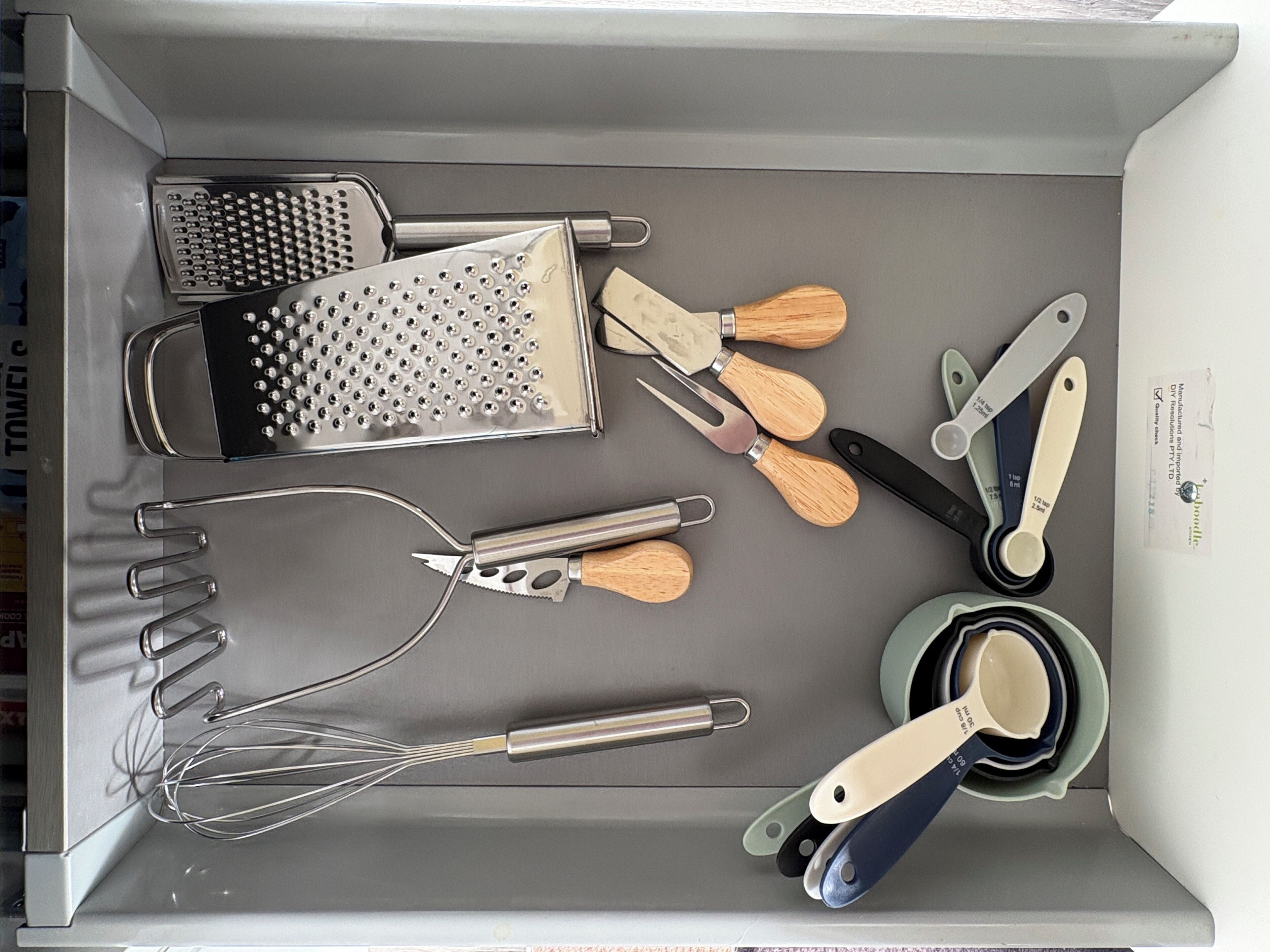 A kitchen drawer with various utensils including a grater, whisks, spatulas, and measuring spoons.