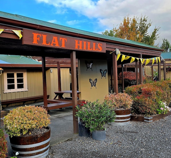 A building with a sign reading 'FLAT HILLS' and a covered patio area with potted plants.