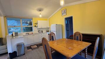 A compact kitchen with white cabinets, a dining table with blue upholstered chairs, and a window with a view of trees.