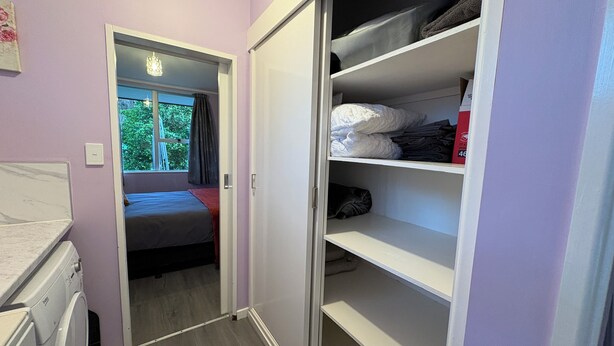 Uma área de lavanderia com máquina de lavar, cama e armário com prateleiras.