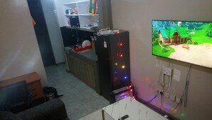 Ett vardagsrum med en soffa, en tv som hänger på väggen, ett kylskåp och ett köksområde i bakgrunden.