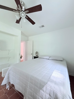 Ein Schlafzimmer mit einem Bett, einem Deckenventilator, einem Nachttisch und einer Tür zu einem anderen Raum.