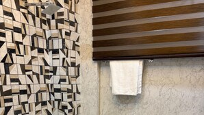 Casa de banho com parede de azulejos geométricos, chuveiro, sanita e lavatório.