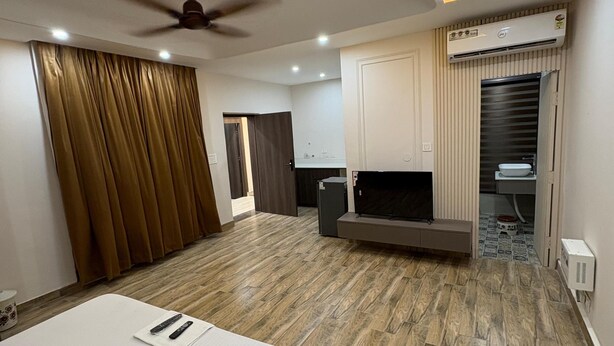 Quarto de hotel moderno com uma cama grande, ventilador de teto, iluminação embutida, ar condicionado integrado e uma pequena cozinha.