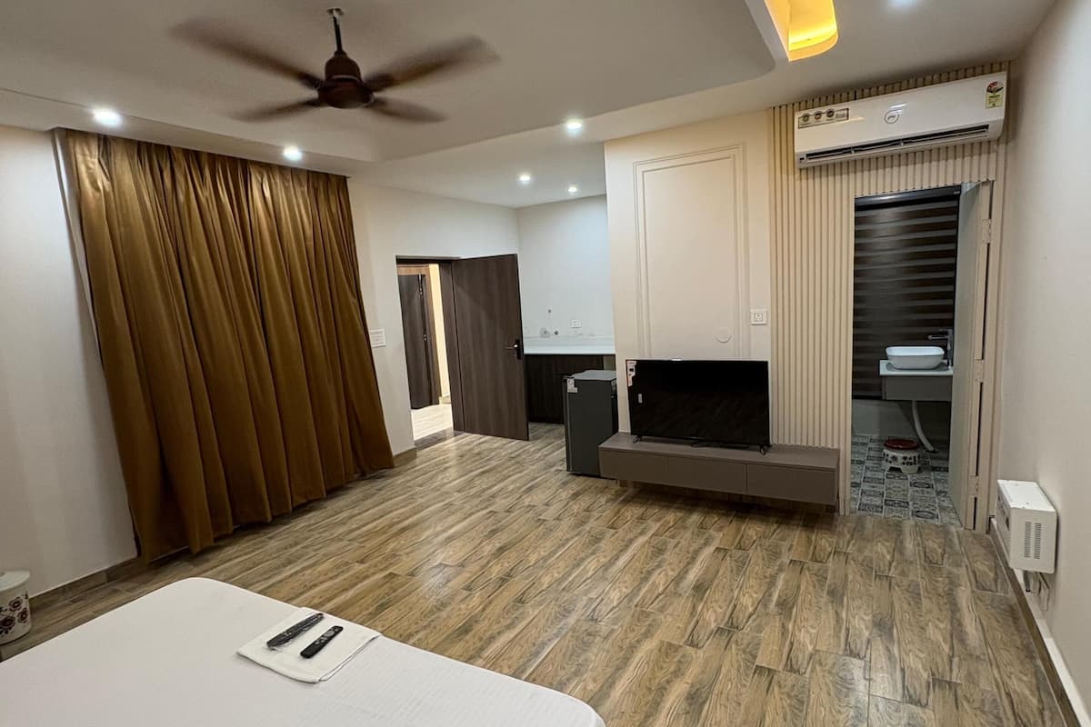 Quarto de hotel moderno com uma cama grande, ventilador de teto, iluminação embutida, ar condicionado integrado e uma pequena cozinha.
