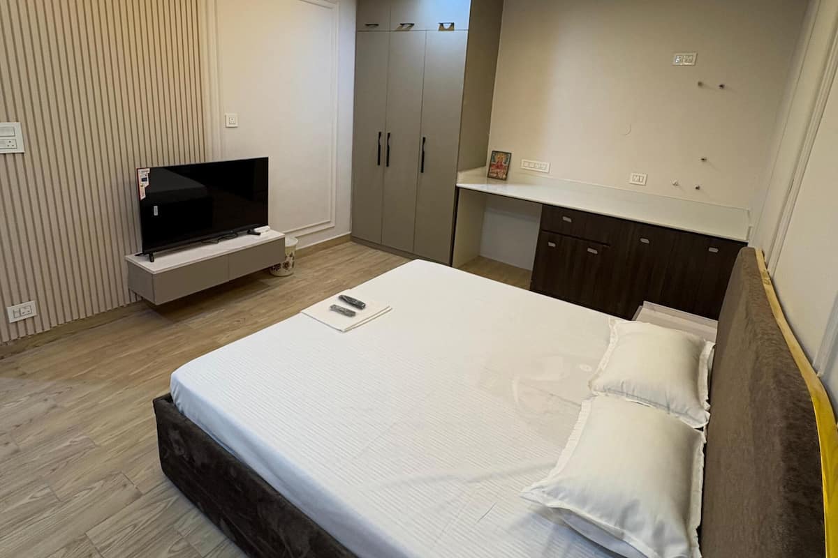 Quarto moderno com cama, televisão, guarda-roupa e ventoinha no teto.