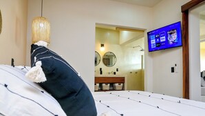 Una camera da letto con un letto, una televisione montata a parete, una lampada a sospensione e un bagno visibile tramite una porta aperta.