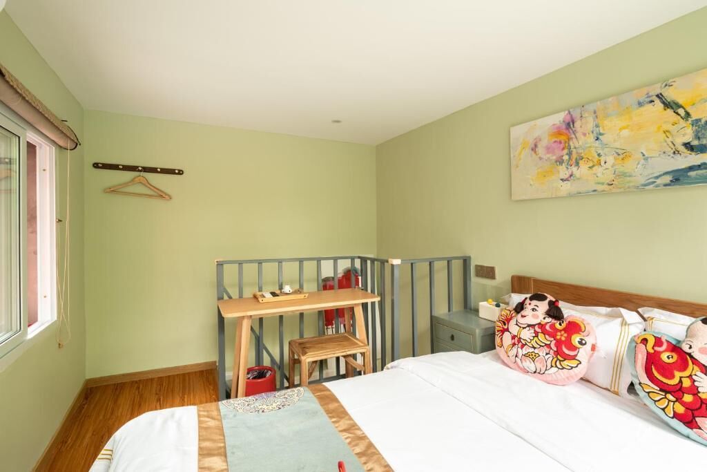 Un dormitorio con cama, escritorio, silla, perchero y un cuadro en la pared.