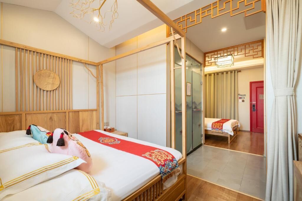 A hotel room with a wooden bed, a mirror, a red door, and a traditional Asian-style wall panel.