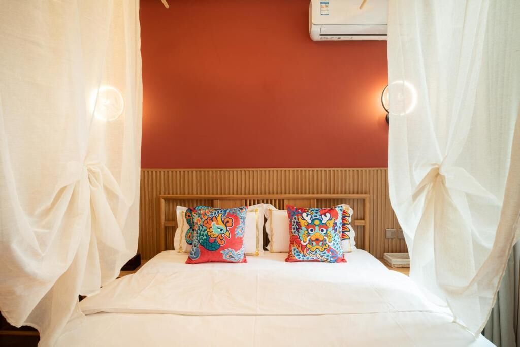 A bed with two colorful pillows, a wooden headboard, and a white curtain.