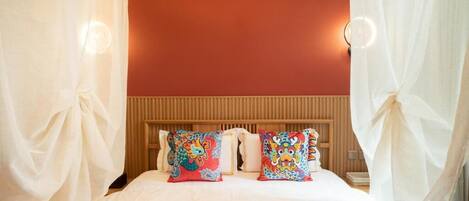 A bed with two colorful pillows, a wooden headboard, and a white curtain.
