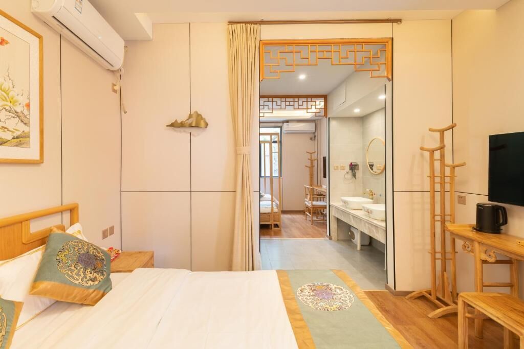 A hotel room with a bed, a wooden side table, a television, a mirror, and a bathroom visible through an open door.