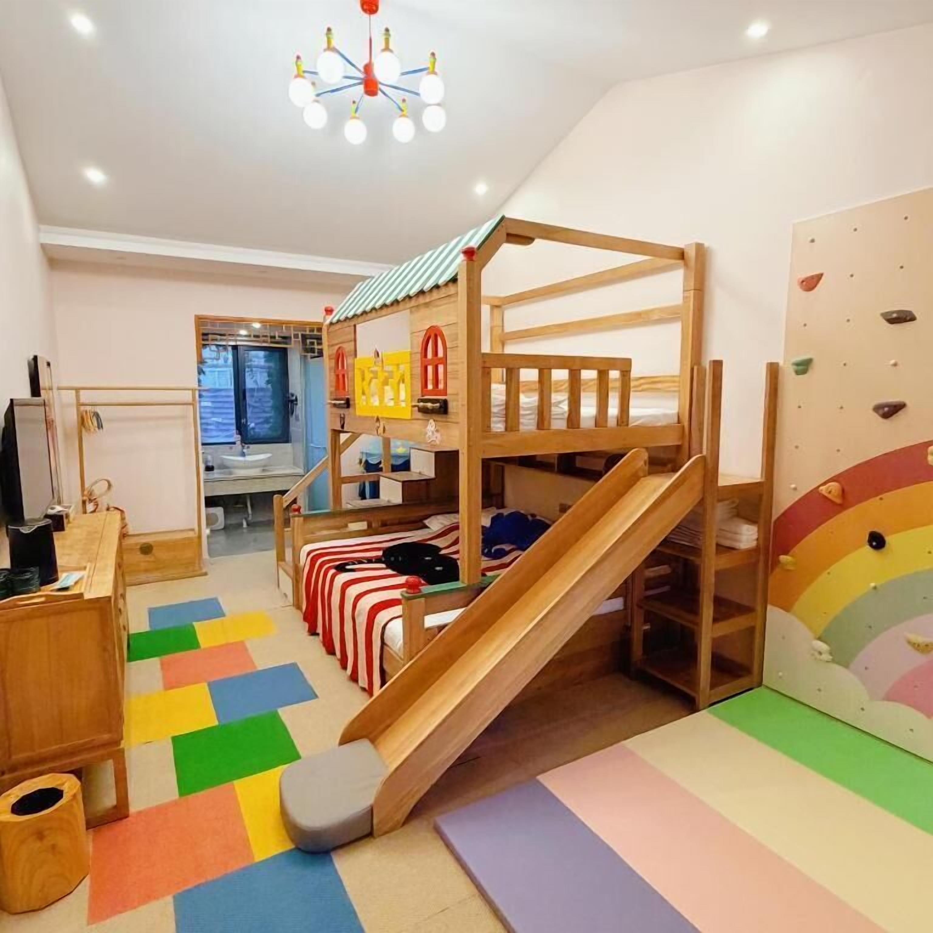 Un cuarto de juegos infantil con literas, un tobogán, una pared de escalada y un suelo colorido.