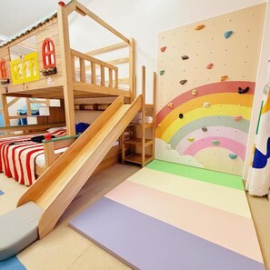 Ein Stockbett mit Rutsche, Kletterwand und Wandgestaltung im Regenbogen-Design.