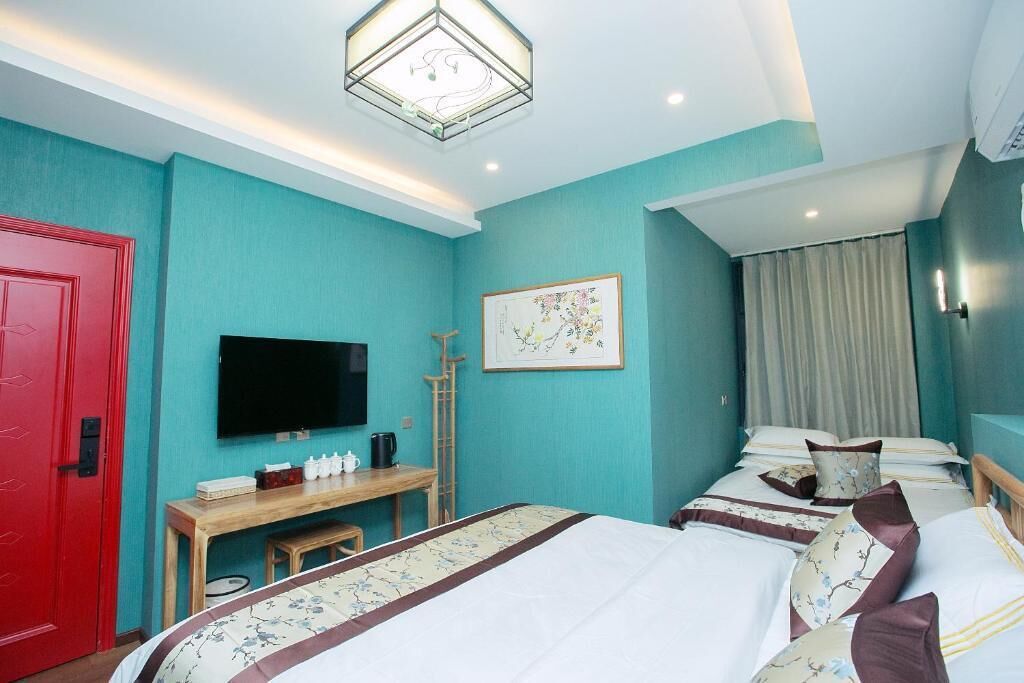 Una habitación de hotel con paredes color turquesa, una puerta roja, un televisor de pantalla plana, un escritorio con una silla y dos camas con ropa de cama estampada.