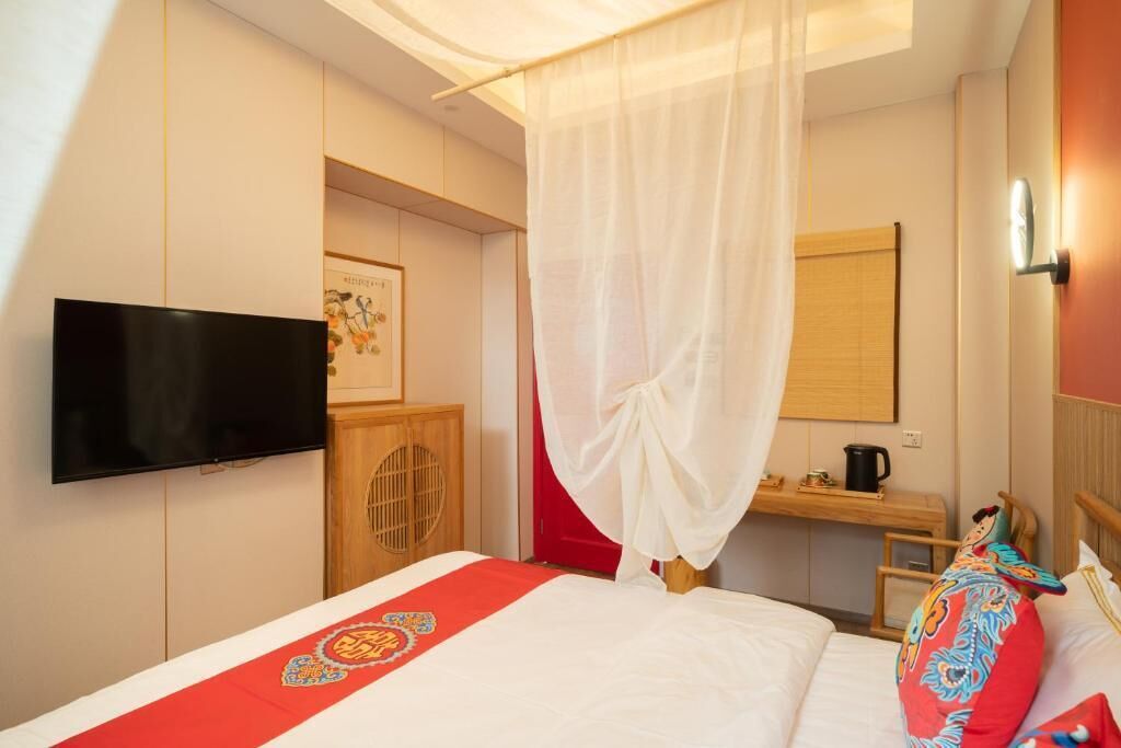 Una habitación de hotel con cama, televisión, escritorio y ventana con cortina.