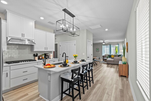 A modern kitchen with white cabinets, a central island with bar stools, a stainless steel range hood, and a pendant light.