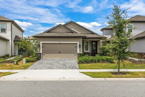 A residential house with a garage, driveway, and a small tree in the front yard. - Luxury Villa w/ Pool & Gym Near Disney (Kissimmee)