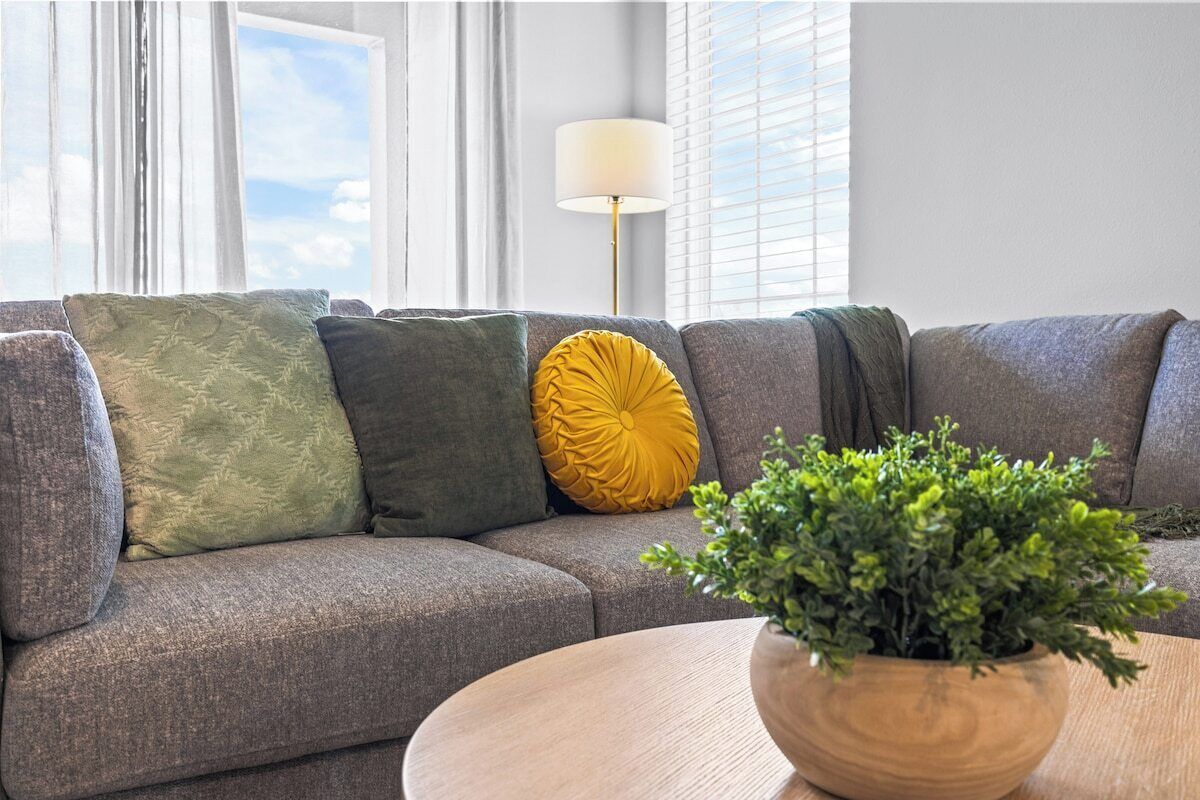 A grey sofa with patterned cushions, a yellow accent pillow, and a wooden side table with a green plant.