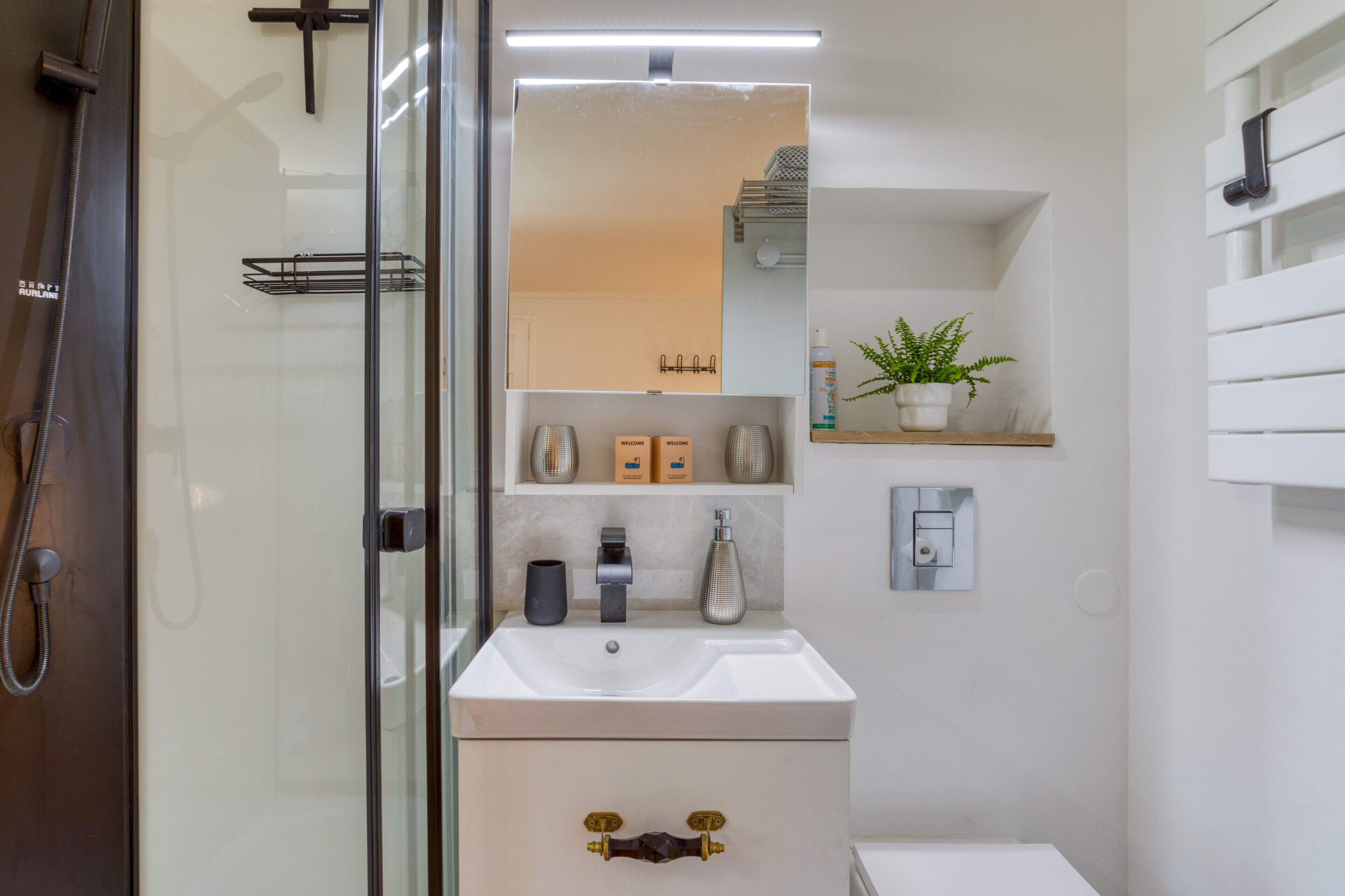 Ein modernes Badezimmer mit einer Duschkabine aus Glas, einem weißen Waschbecken, einem Spiegel und einer kleinen Ablage mit Pflegeprodukten.