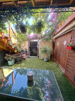 Een tuin met een glazen tafel, planten in potten en een houten omheining.