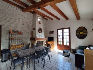 A dining area with a table and chairs, a fireplace, a wooden ceiling, and a brick wall. - Maison de la Boirie (Saint-Denis-d'Oléron)
