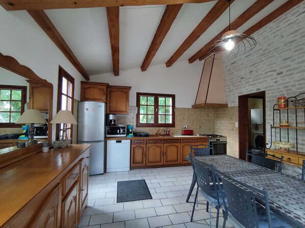A kitchen with wooden cabinets, a refrigerator, a stove, and a dining table with chairs. - Maison de la Boirie (Saint-Denis-d'Oléron)
