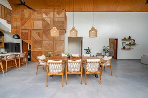Ein moderner Essbereich mit Holztisch und -stühlen, Pendelleuchten und einem geometrischen Wanddesign.