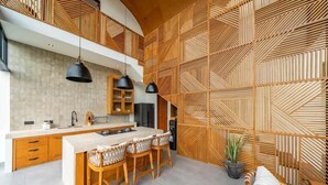 Een moderne keuken met een centraal eiland, houten kastjes, hanglampen en een muur met een geometrisch patroon.