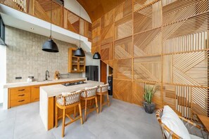 Eine moderne Küche mit einer zentralen Kochinsel, Holzschränken, Pendelleuchten und einer Wand mit geometrischem Muster.