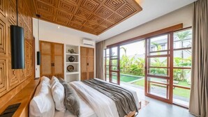 Een slaapkamer met een groot bed, houten plafond en uitzicht op een tuin via een schuifdeur.