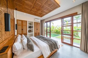 Ein Schlafzimmer mit einem großen Bett, Holzboden und Blick auf einen Garten durch eine Schiebetür.