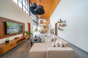 Ein geräumiger Wohnbereich mit einem großen Flachbildfernseher, einem Sofa, einem Couchtisch und einer Treppe, die in ein Obergeschoss führt.