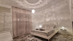 A bedroom with a bed, curtains, a hanging light, and a bedside table. - Repubblica Rooms (Bari)