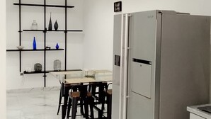 Eine moderne Küche mit Marmorboden, einem Essbereich mit Stühlen, einem Kühlschrank und einem Regal mit Dekoration.