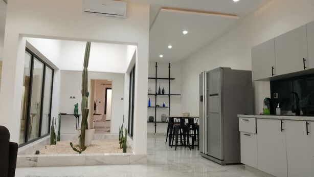 Eine moderne Küche mit integriertem Kühlschrank, ein Essbereich mit Tisch und Stühlen sowie ein Wohnbereich mit Couchtisch und Pflanzen.