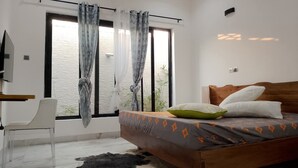 Ein Schlafzimmer mit einem Bett, einem Sessel, einem Schreibtisch und einem Fenster mit Vorhängen.