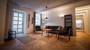 Uma sala de estar ampla com padrão de piso em padrão herringbone, um conjunto de sofás, uma mesa de centro e uma luminária pendente.