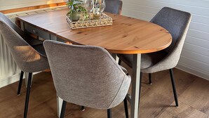 A dining area with a wooden table, grey upholstered chairs, a woven pendant light, and framed floral artwork on the wall. - Coastal Bliss Holiday Home on the Großer Meer in East Frisia (Südbrookmerland)