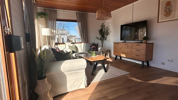 A modern living room with a sofa, coffee table, TV, wooden cabinet, and large windows. - Coastal Bliss Holiday Home on the Großer Meer in East Frisia (Südbrookmerland)