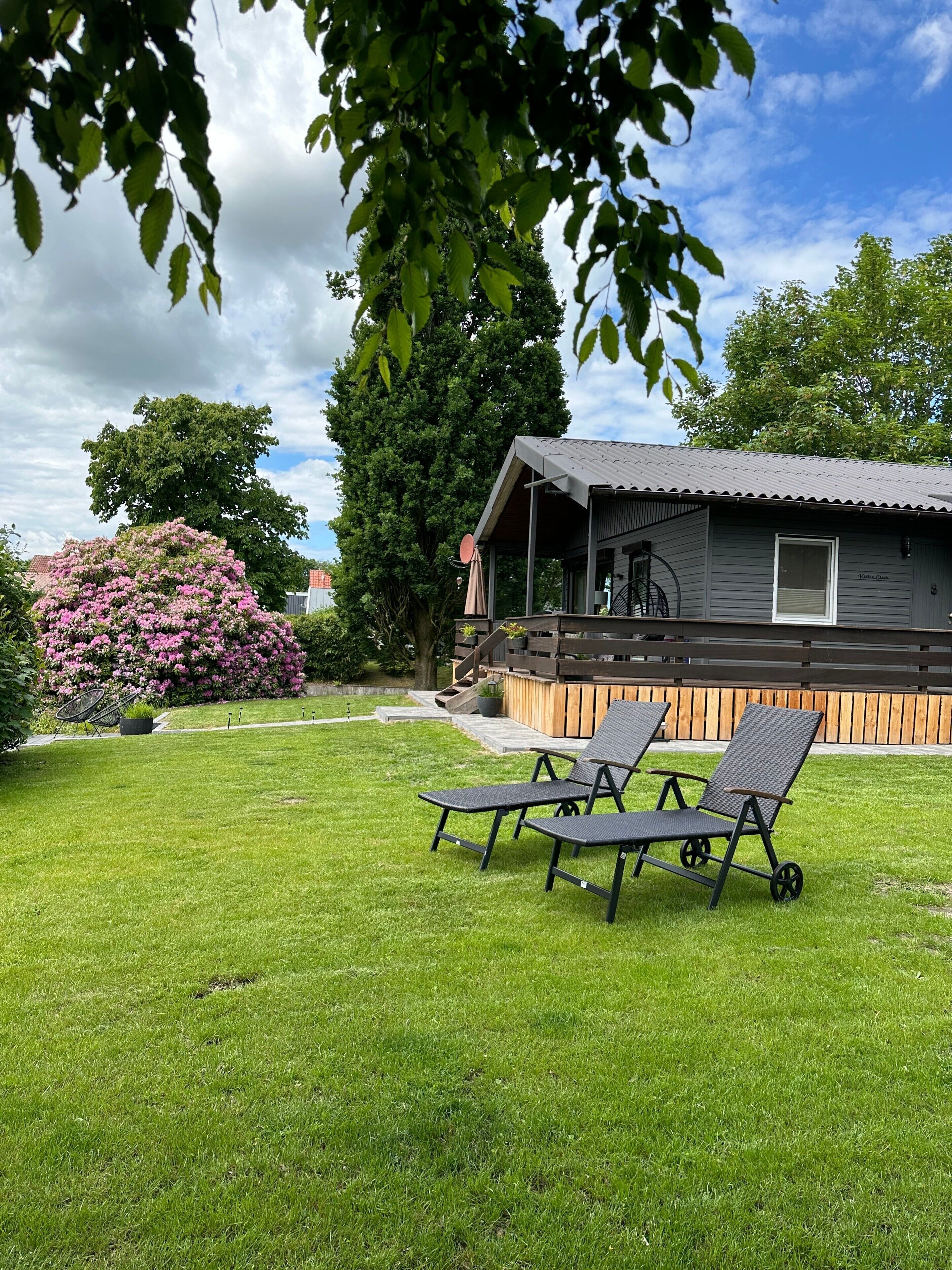 A modern house with a covered porch, a lawn, and two lounge chairs.