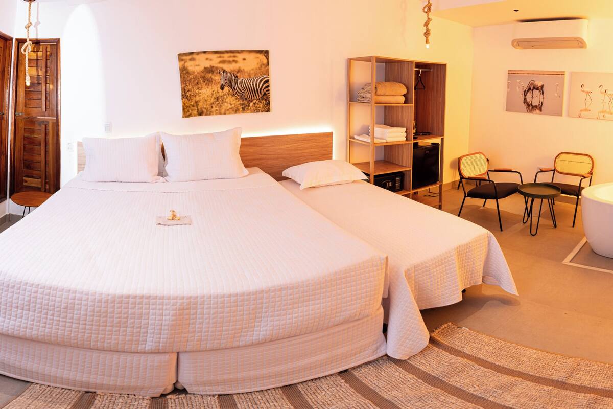 A hotel room with a large bed, a desk, a chair, a wardrobe, a bathroom with a bathtub, and artwork on the walls.