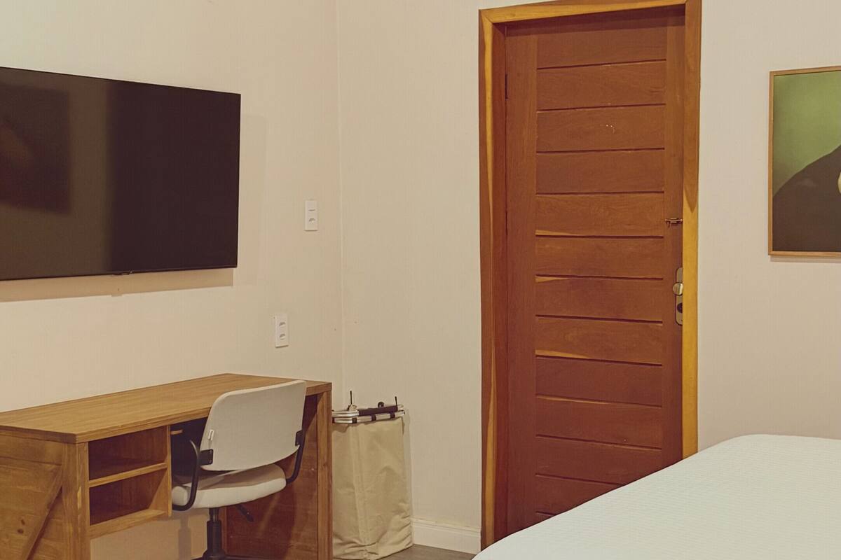 A bedroom with a bed, a desk with a chair, a television, and a wooden door.