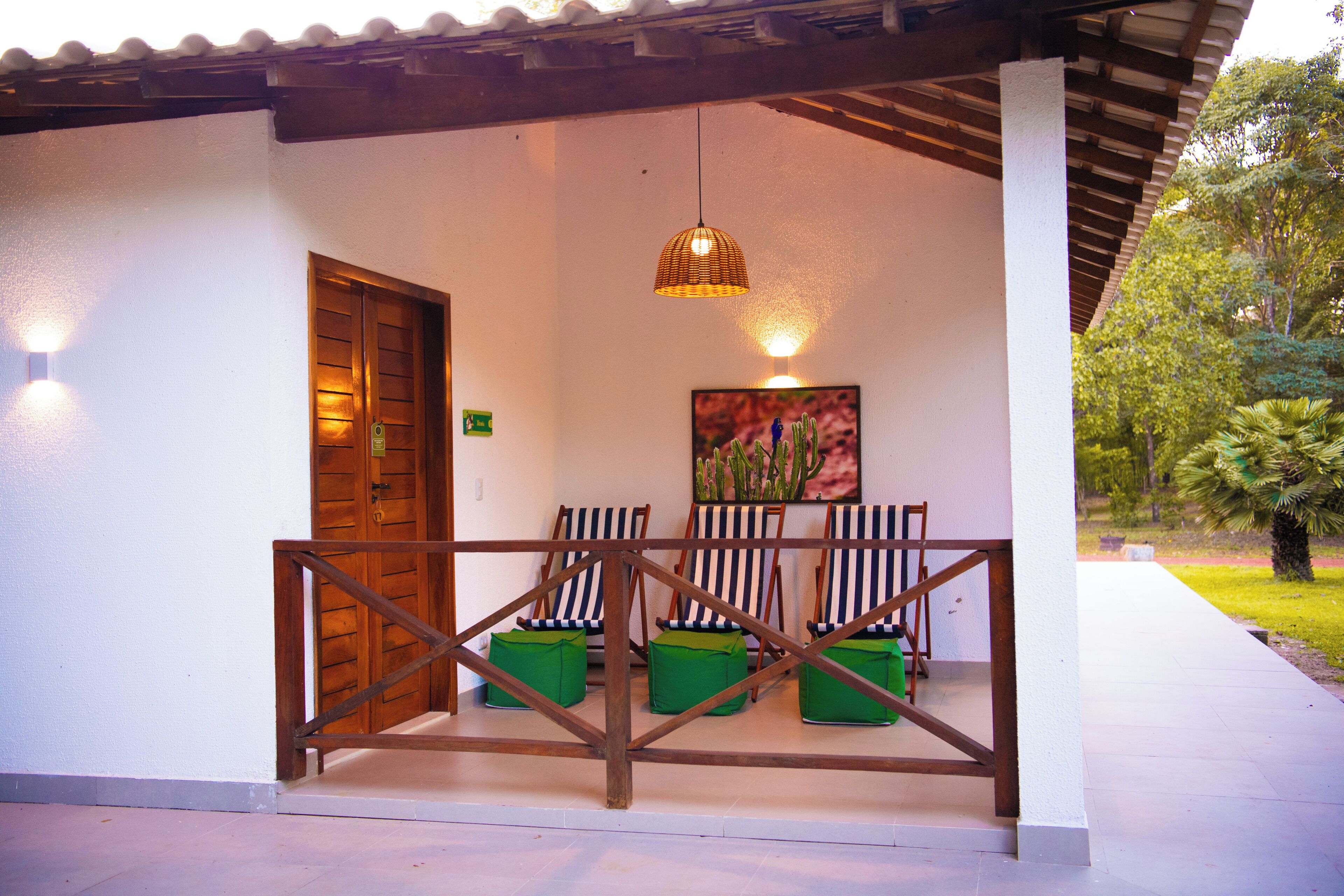 A covered outdoor seating area with a wooden railing, a door, and a hanging light fixture.
