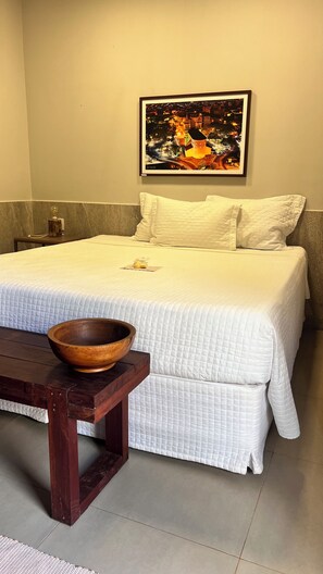 A neatly made bed with white bedding, a wooden bowl on a table, and a framed picture on the wall. - Nazareth Eco Hotel (José de Freitas)