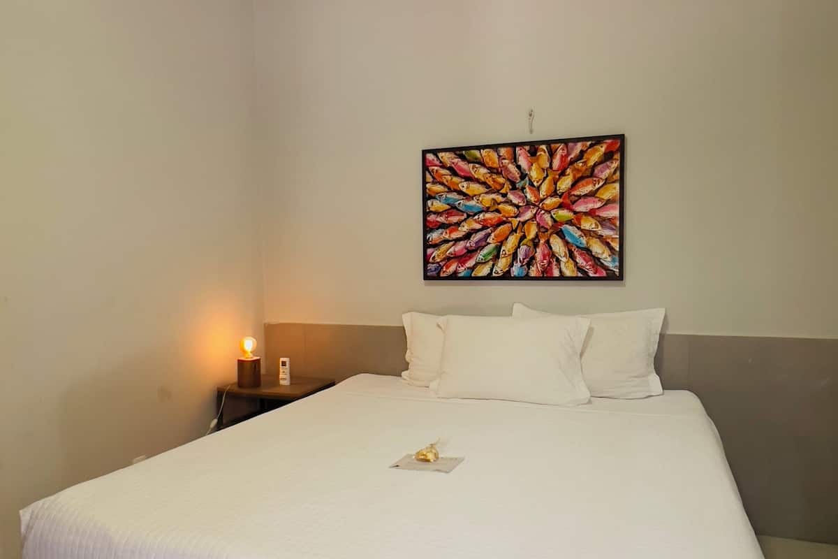 A hotel room with a large bed, a nightstand with a lamp, and a colorful abstract painting on the wall.