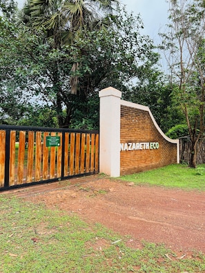 A gated entrance with a sign reading 'NAZARETH ECO' and a signboard for 'ATENÇÃO' with a date and time.
